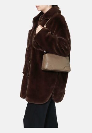 Cappotto in pelliccia sintetica marrone con colletto, vestibilità over e bottoni grandi; abbinato a una borsa in taupe testurizzato tenuta dalla persona.