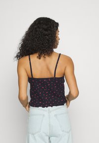 Top de alças fina em azul-marinho com padrão floral, apresentando pequenas flores vermelhas em um tecido texturizado e uma bainha franzida.