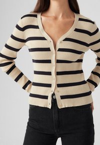 Beżowo-granatowy prążkowany kardigan w paski z dekoltem w serek, długimi rękawami i guzikami z przodu. Charakteryzuje się dopasowanym krojem i teksturowaną tkaniną.