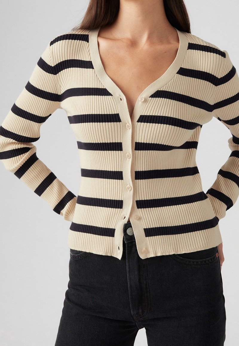 Beżowo-granatowy prążkowany kardigan w paski z dekoltem w serek, długimi rękawami i guzikami z przodu. Charakteryzuje się dopasowanym krojem i teksturowaną tkaniną.