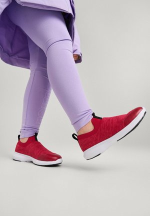 Czerwone buty wsuwane z teksturowanym wierzchem, z czarną pętelką na pięcie oraz białą podeszwą, w połączeniu z jasnopurpurowymi legginsami.