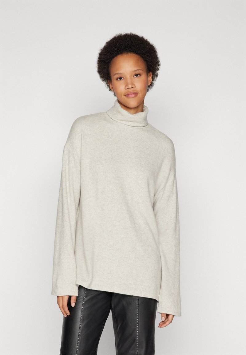 Light gray turtleneck sweater in soft knit fabric, featuring a relaxed fit and long sleeves, paired with black pants with vertical stitching.
