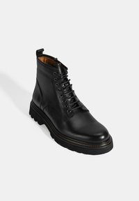 Zwarte leren enkelboot met een ronde neus, vetersluiting aan de voorkant, gestructureerde zijkanten en een robuuste zool met contrasterende stiksels.