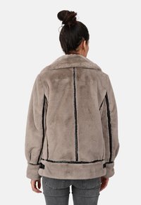 Ljusgrå faux fur-jacka med bred krage, svarta accent-sömmar och en avslappnad passform. Har sidogylfar och manschettdetaljer.