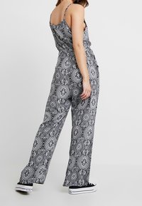 Combinaison à motifs noir et blanc avec jambes larges, bretelles spaghetti et coupe décontractée. Portée avec des baskets noires ; présente des dessins complexes.