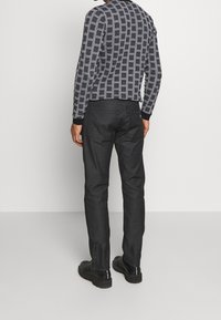 Svart och vit rutiga långärmad skjorta med ribbade manschetter, matchad med åtsittande svarta byxor och svarta stövlar. Minimalistisk design, slät textur.