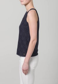 Granatowy top bez rękawów z koronkowymi detalami z przodu, okrągłym dekoltem i klasycznym krojem. W połączeniu z białymi dopasowanymi spodniami.