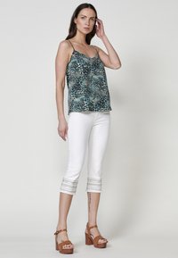 Camisola a fiori con spalline sottili, abbinata a pantaloni bianchi a culotte con bande metalliche all'orlo e sandali con zeppa marroni.