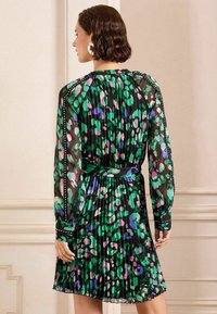 Rochie plisată verde și neagră cu un model floral abstract multicolor, mâneci lungi din material transparent și un cordon din țesătură la talie.