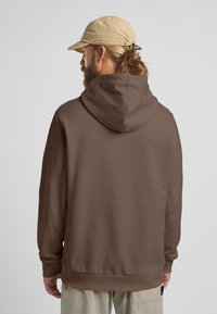 Felpa marrone con vestibilità ampia, dotata di un ampio cappuccio e polsini a coste. Il tessuto appare liscio e morbido, con un design minimalista.