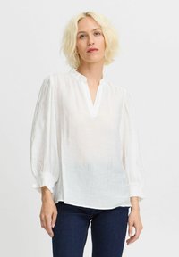 Vit, lätt blus med v-ringning, rynkade ärmar och strukturerad tyg. I kombination med mörkblå jeans.