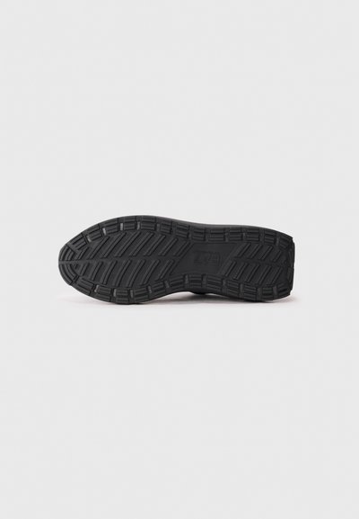 Semelle extérieure de sneaker noire avec une surface texturée et patinée ; présente des rainures profondes pour l'adhérence et des détails de renforcement pour la durabilité.