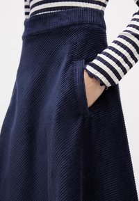 Marinblå kordflorskjol med vertikal ribbning, hög midja och sidofickor. Accentuerad med en fint ribbad och vågig ärm.