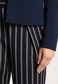 Blazer marine avec finition texturée associé à un pantalon rayé vertical noir et blanc avec un pli marqué et des poches latérales.