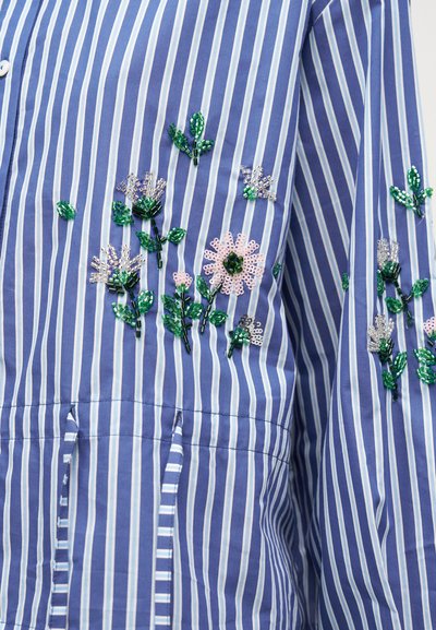 Tissu à rayures bleu et blanc avec broderie florale perlée verte et rose sur la manche et la poitrine d'une chemise.