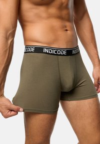 Olívazöld boxer szexi anyagból, fekete derékrésszel, amelyen a "INDICODE" márkaneve fehér betűkkel szerepel, testhezálló fazon.