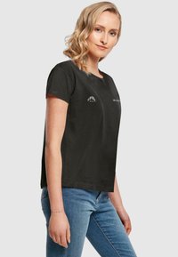 Sort crew-neck t-shirt med korte ærmer, der har diskrete tekstlogoer trykt på forsiden. Blødt bomuldsstof og afslappet pasform.