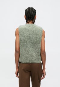 Bezrukávová, svetlozelená fleecová vesta s textúrovaným vonkajším povrchom. Rovný strih, zaoblený výstrih a žiadne viditeľné kovové časti. Jednoduchý dizajn.
