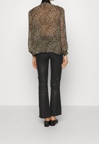 Blusa de gasa con estampado de leopardo y cuello negro, con mangas voluminosas. Combinada con pantalones negros ajustados y acampanados y zapatos oscuros.