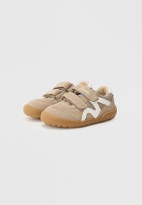 Adidași bej cu benzi Velcro, părți laterale din plasă și tălpi din cauciuc; includ accente albe și o parte superioară texturată pentru respirabilitate.