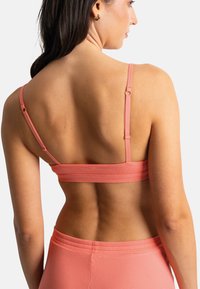 Soutien-gorge de sport côtelé, rose clair, avec des bretelles ajustables. Présente un ajustement près du corps, un design sans couture et une surface lisse et texturée.