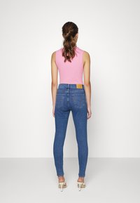 Jeans de mezclilla de color azul ajustados y de cintura alta, con bolsillos traseros y un parche de cuero marrón claro en la cinturilla. Combinados con una blusa sin mangas de color rosa.