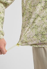 Chemise à manches longues légère avec un motif moucheté de vert, beige et noir, dotée d'un ourlet à cordon de serrage ajustable et d'une texture douce.