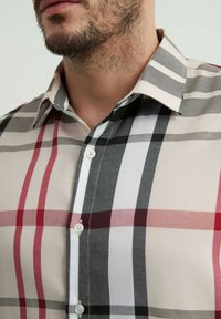 Chemise à carreaux en beige, rouge, noir et blanc. Tissu en coton avec des lignes nettes et contrastées. Dotée d'un col classique et d'une fermeture à boutons.