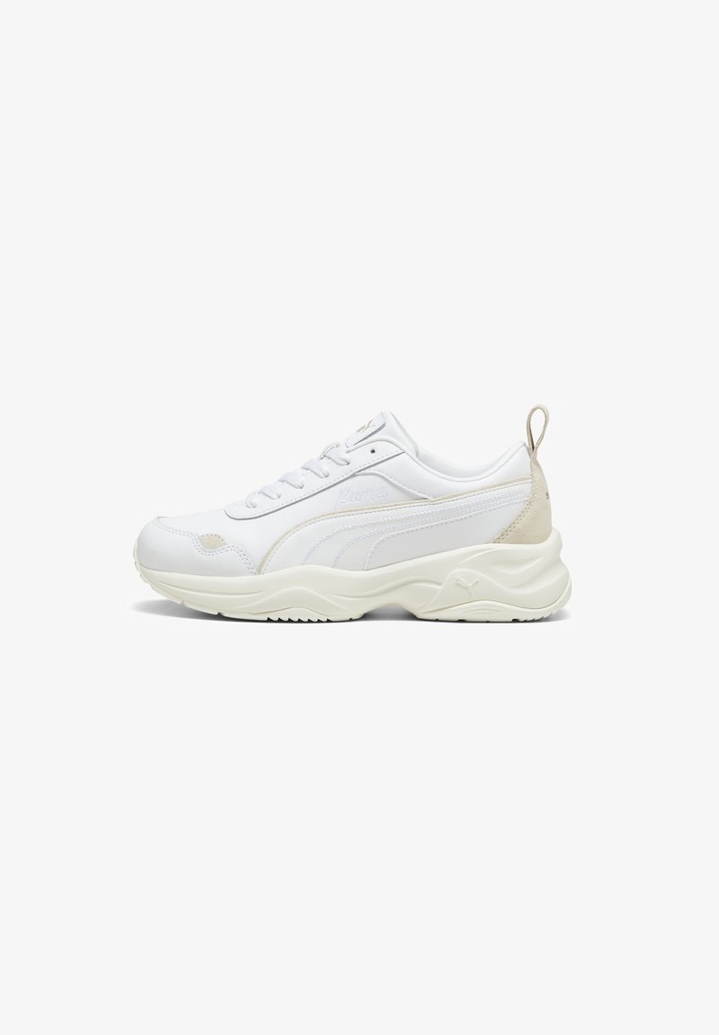 Sneaker Puma blanche avec des accents beiges, fermeture à lacets, semelle texturée et languette au talon, présentée de côté sur fond blanc.