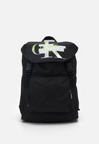 Mochila negra hecha de un tejido duradero, con una gran solapa que presenta un estampado gráfico en blanco y verde neón, un bolsillo frontal con cremallera y correas ajustables.