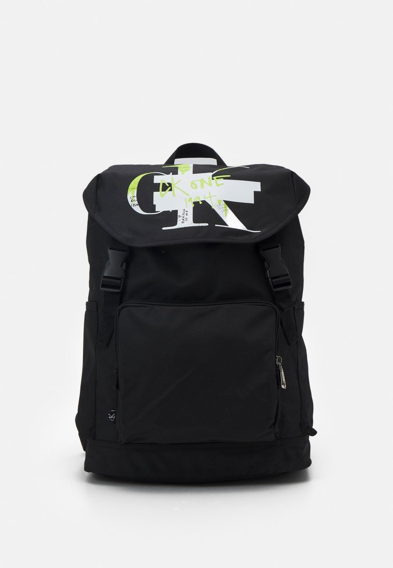 Mochila negra hecha de un tejido duradero, con una gran solapa que presenta un estampado gráfico en blanco y verde neón, un bolsillo frontal con cremallera y correas ajustables.