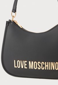 Melnas ādas plecu soma izliekta forma, ar zelta piederumiem un iepresētiem "LOVE MOSCHINO" burtiem priekšpusē. Ar rāvējslēdzēju aizdari augšdaļā.