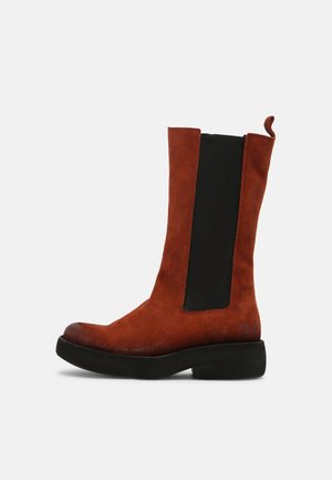 Bottines en suède marron avec un panneau élastique noir, bout arrondi et semelle noire basse. Elles sont dotées d'une languette à l'arrière pour un enfilage facile.