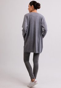 Grijze lange mouwen cardigan met een losse pasvorm, gestructureerd breiwerk, zijzakken, in combinatie met grijze slim fit jeans en witte schoenen met roze accenten.