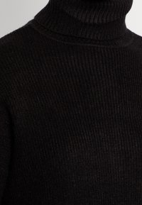 Maglione nero a collo alto con texture a costine. Materiale morbido e lavorato a maglia, con un alto colletto e un design aderente, che enfatizza calore e comfort.