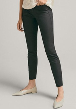 Person wearing black slim-fit ankle pants and beige pointed-toe flats, standing against a plain light background.