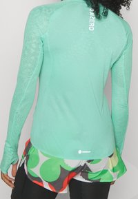 Mintgrünes langärmeliges Sportoberteil mit strukturiertem Muster, ausgestattet mit dem "ADIZERO"-Logo auf dem Rücken und Daumenlöchern an den Bündchen.