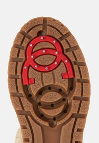 Podešev boty z opálené gumy s dezénem, s červenými akcenty ve vrstvách překrývajících se kruhových tvarů a malými ozdobnými cvočky.