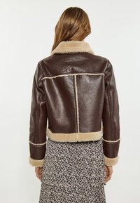 Brązowa skórzana kurtka o krótkim kroju z kołnierzem i wykończeniem z futerka, o gładkiej fakturze i poziomych szwach na plecach.