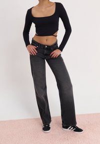 Svart långärmad kort topp med fyrkantig halsringning, parat med mörkgrå vida jeans och svarta sneakers med vita ränder.