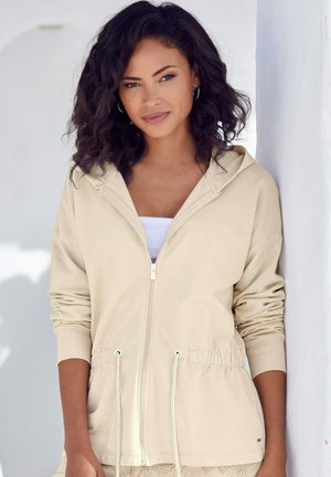 Beige Zip-Hoodie mit Kordelzugbund, gerippten Bündchen und einer weichen Stofftextur. Mit Kapuze und einem Frontreißverschluss.