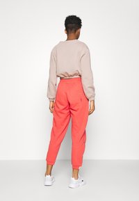 Pink sweatpants with a tapered leg and elastic waistband. Light beige long-sleeve top with fitted cuffs. White sneakers complete the outfit.