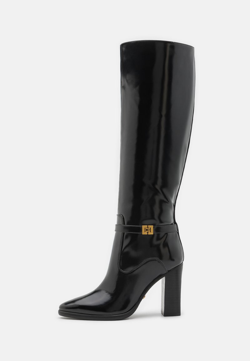 Botas de charol negras hasta la rodilla con punta afilada, acento en hardware dorado y un tacón grueso. Superficie lisa y brillante con un detailing mínimo.