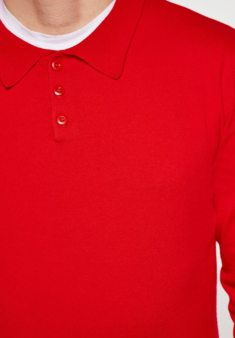 Polo shirt rossa realizzata in tessuto morbido, con colletto classico, patta con tre bottoni e texture a coste. Nessun motivo o accento visibile.