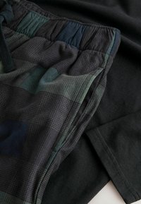Pantalones cortos negros con un patrón de cuadros verde y marino, que cuentan con una cintura elástica y un tejido texturizado. Camiseta negra lisa por debajo.
