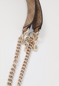 Vihreä kuvioitu kangas olkahihna kullattu ketjuvaruste ja tarrat, joissa on brändättyjä aksentteja ja sileää nahkaista viimeistelyä.