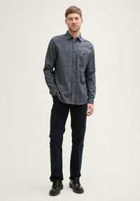 Cămășă gri cu un model texturat, cu un singur buzunar la piept, combinată cu pantaloni închiși la culoare și pantofi negri cu șireturi. Design cu guler plat.