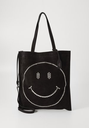 Borsa tote in suede nero con un grande design a faccina sorridente decorato con borchie argentate. Due manici robusti e una tracolla regolabile.
