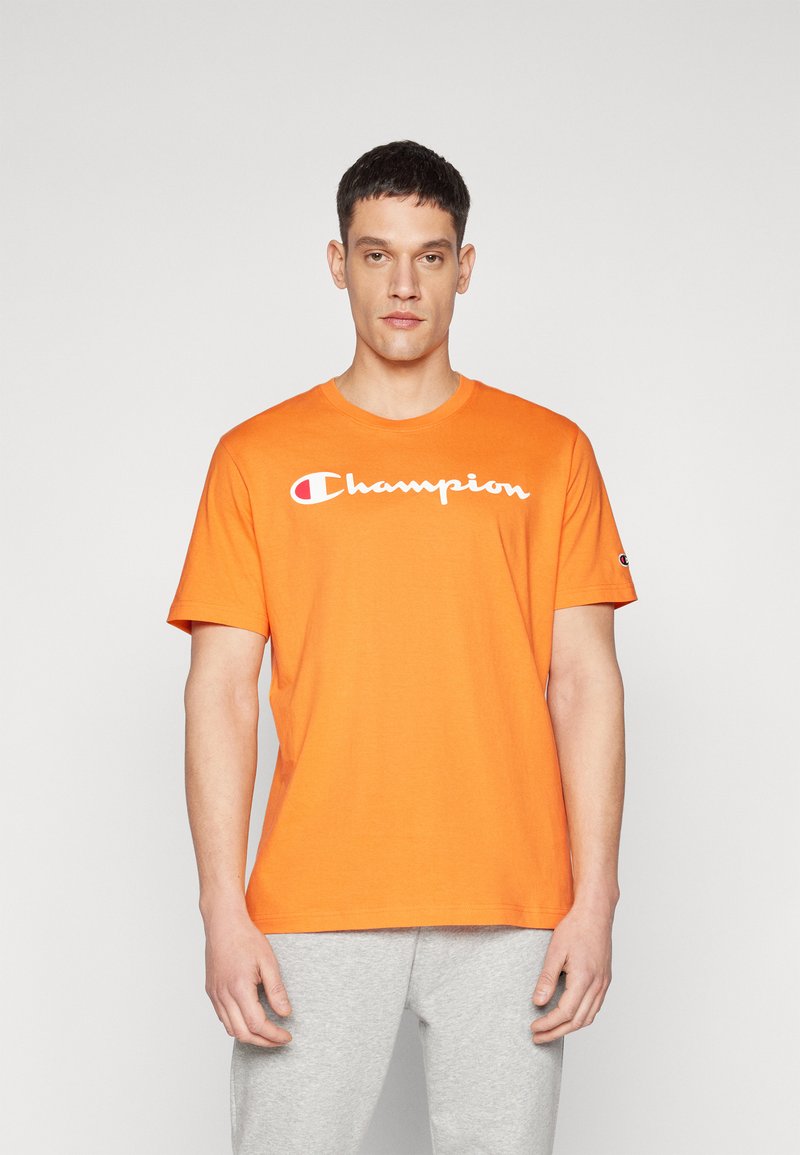 Orange Baumwoll-T-Shirt mit kurzen Ärmeln, das das weiße "Champion"-Logo quer über der Brust trägt. Glatte Textur, runder Halsausschnitt.