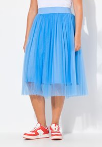 Gonna di tulle azzurro chiaro con una vita spessa, lunghezza fino al ginocchio, design a strati. Abbinata a sneaker rosse e bianche.